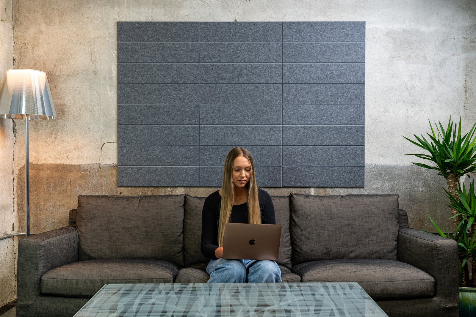 A person sitting on a couch in a room with Felt Right wall shiplap paneling in a shade of grey, using a laptop.