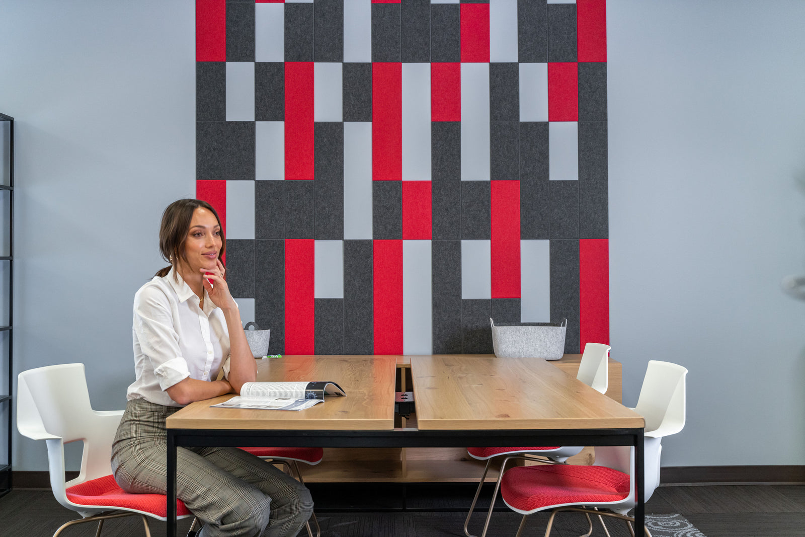 A Felt Right wall art design in shades of pink and black with the negative space of the blue wall popping through in a room with a table and woman sitting there.