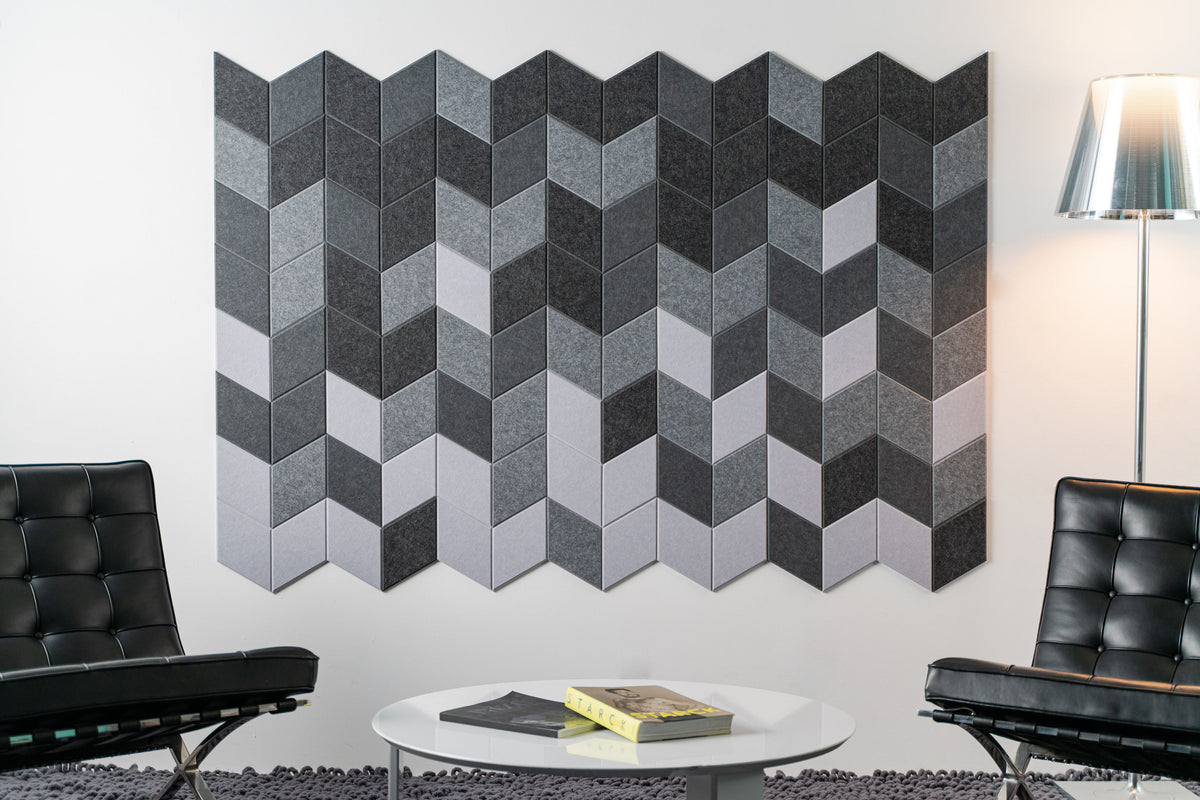 A Felt Right wall art design in shades of grey creating a geometric pattern on a white wall with two chairs and a coffee table.