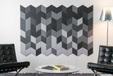 A Felt Right wall art design in shades of grey creating a geometric pattern on a white wall with two chairs and a coffee table.