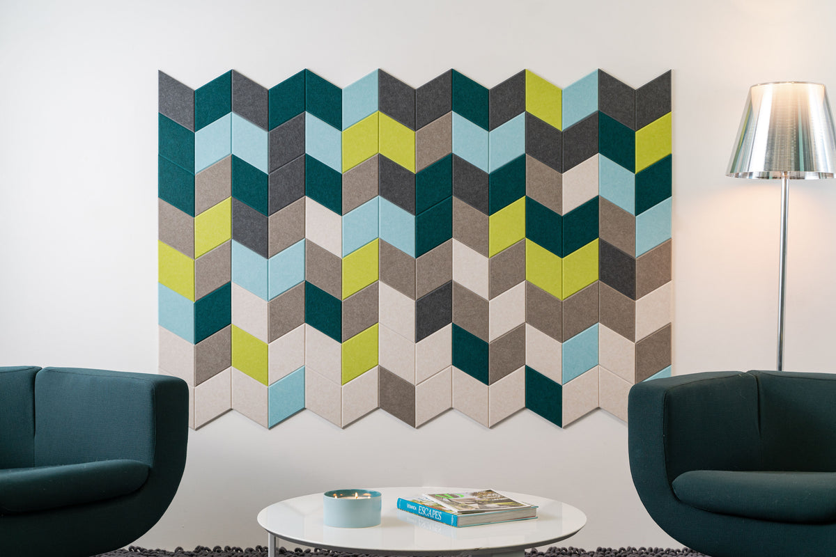 A Felt Right wall art design in shades of blue, green, and greys creating a geometric pattern on an white wall in between two chairs and a side lamp.