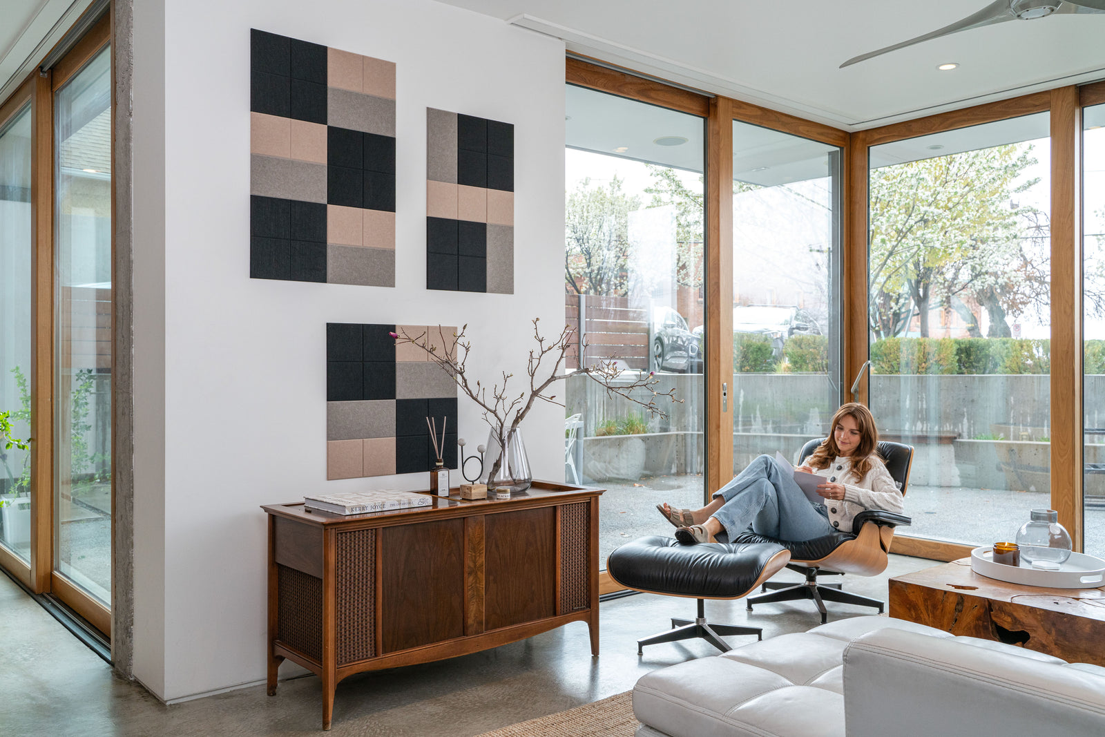 A Felt Right wall art design in shades of black and brown on a white wall in a living room with a girl reading in a chair.