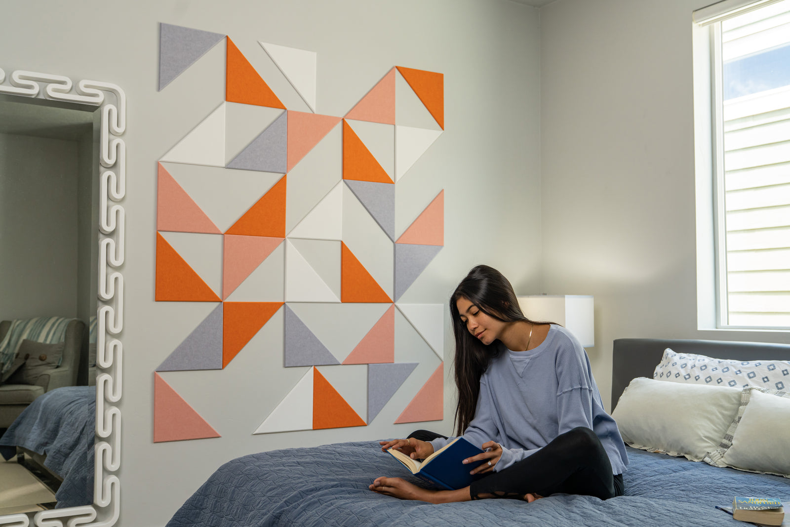 A Felt Right wall art design in shades of orange and grey triangles creating a geometric design on a bedroom wall next to a bed and a mirror.