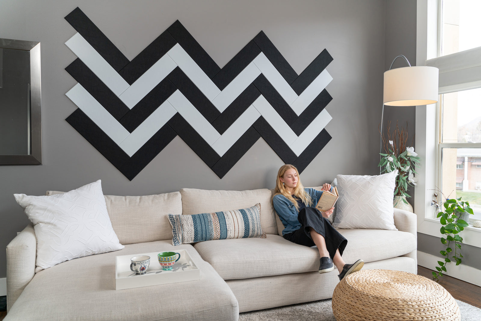 A Felt Right wall art design in black and white making a zig zag pattern on a grey wall with a woman reading on the couch.