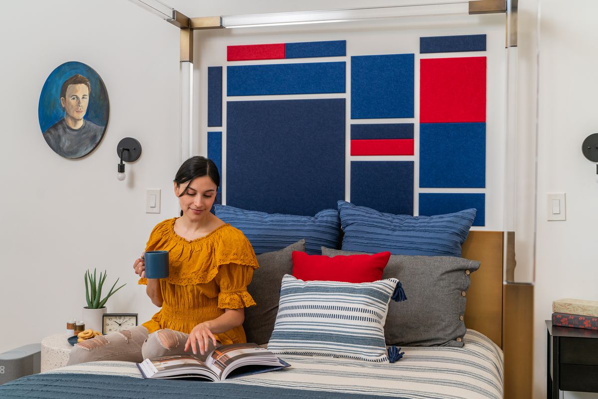 A Felt Right wall art design in shades of blue and red felt tiles as a headboard for a bed on a white wall.