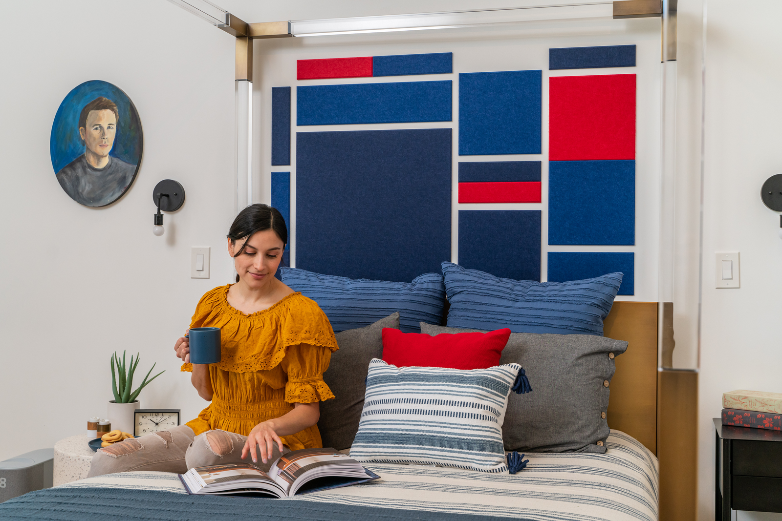 A Felt Right wall art design in shades of blue and red felt tiles as a headboard for a bed on a white wall.