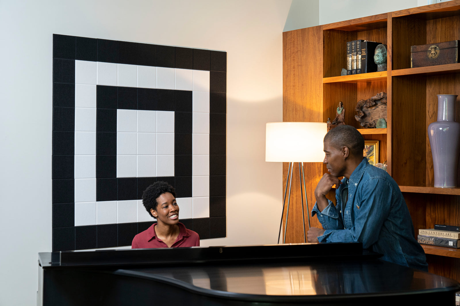 A Felt Right wall art design in shades of Black and white square felt tiles on a white wall with a woman playing the piano.