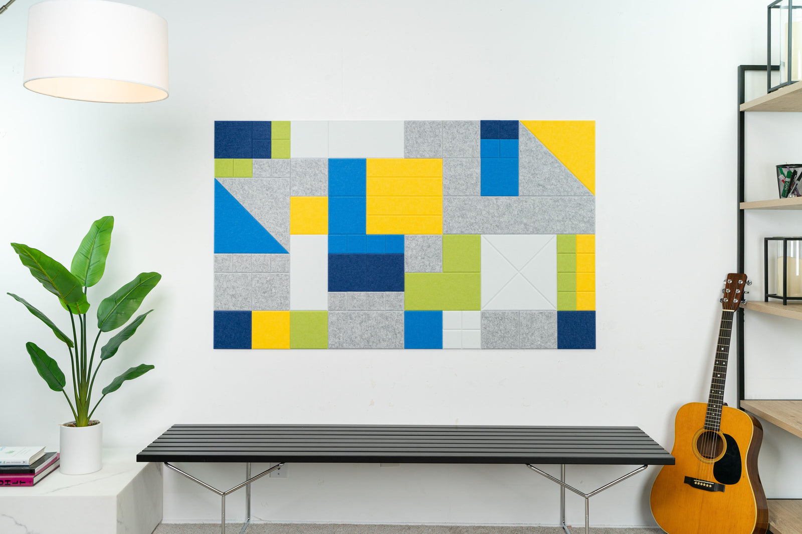 A Felt Right wall art design in shades of grey blue and yellow creating art on a white wall next to a guitar and a shelf and the art placed above a bench.