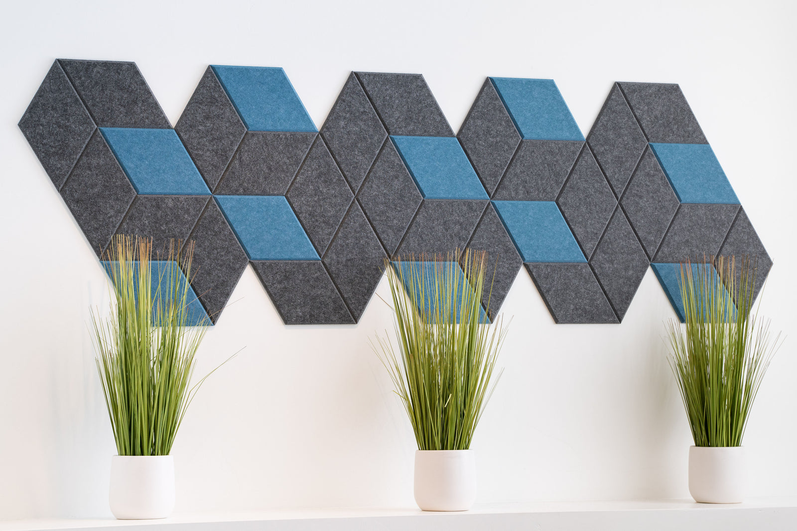A Felt Right wall art design in grey and blue making a geometric shape with three plants in front.