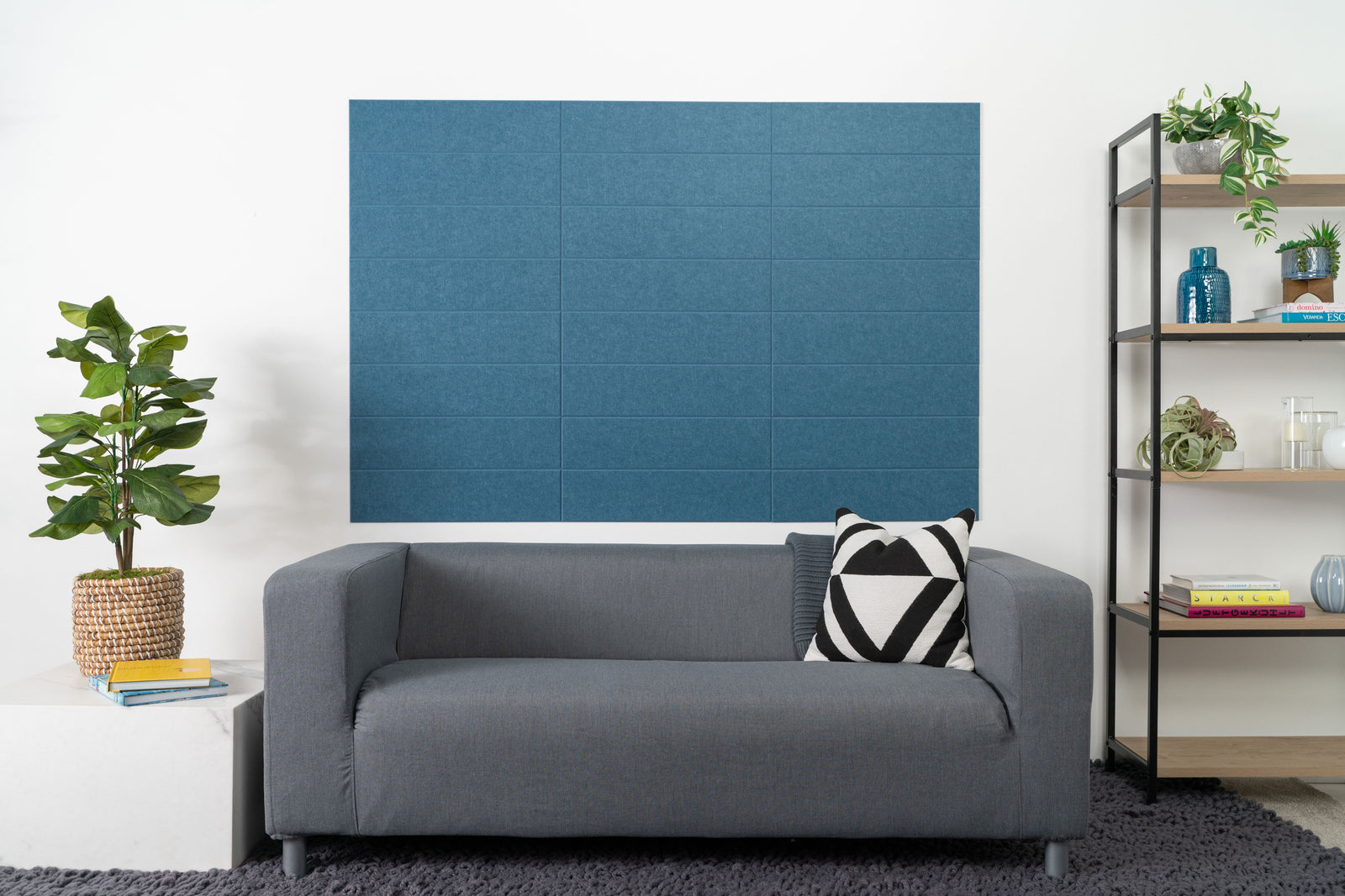 Felt Right Wall design using shiplap blue tiles stacked in a living room above a couch next to a side table with a plant and a bookshelf 