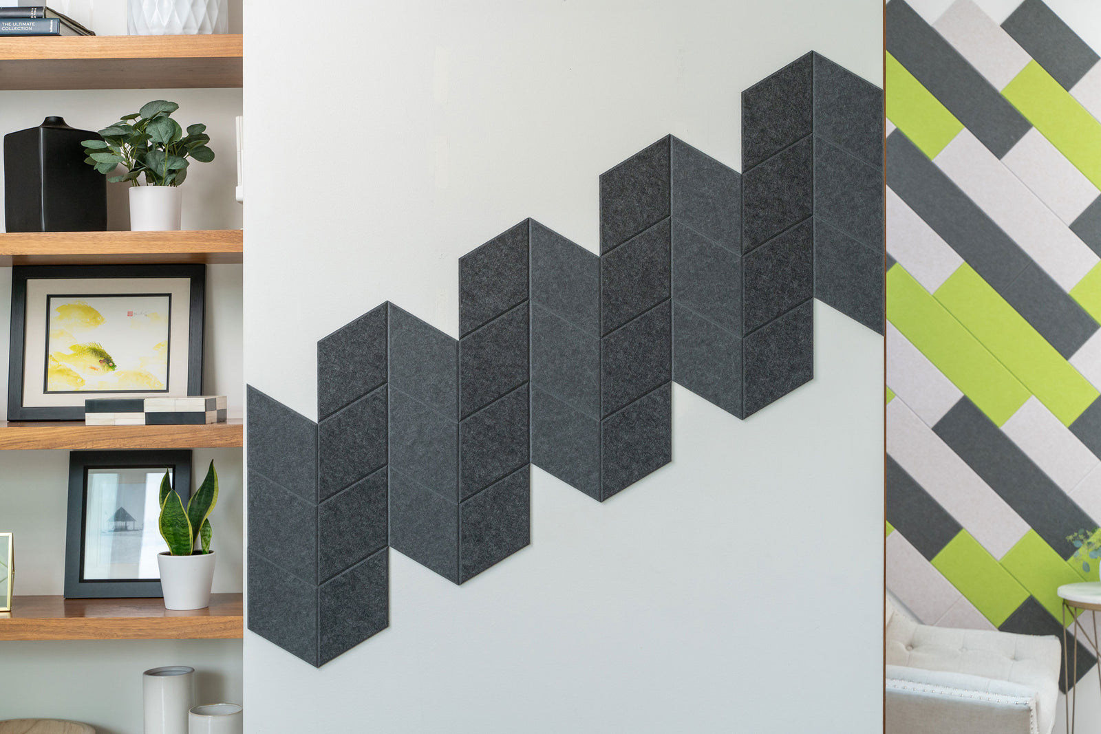 A Felt Right wall art design in shades of black diamond felt tiles on a white wall next to some shelves.
