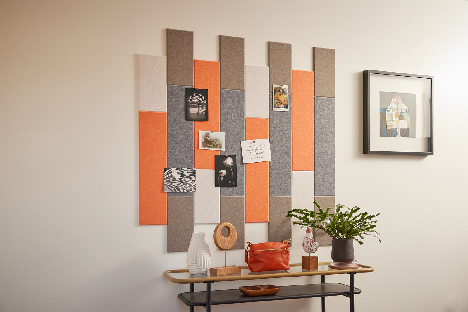 A Felt Right wall art design in orange, browns, and grey of felt that is pinnable on a wall above a side table.