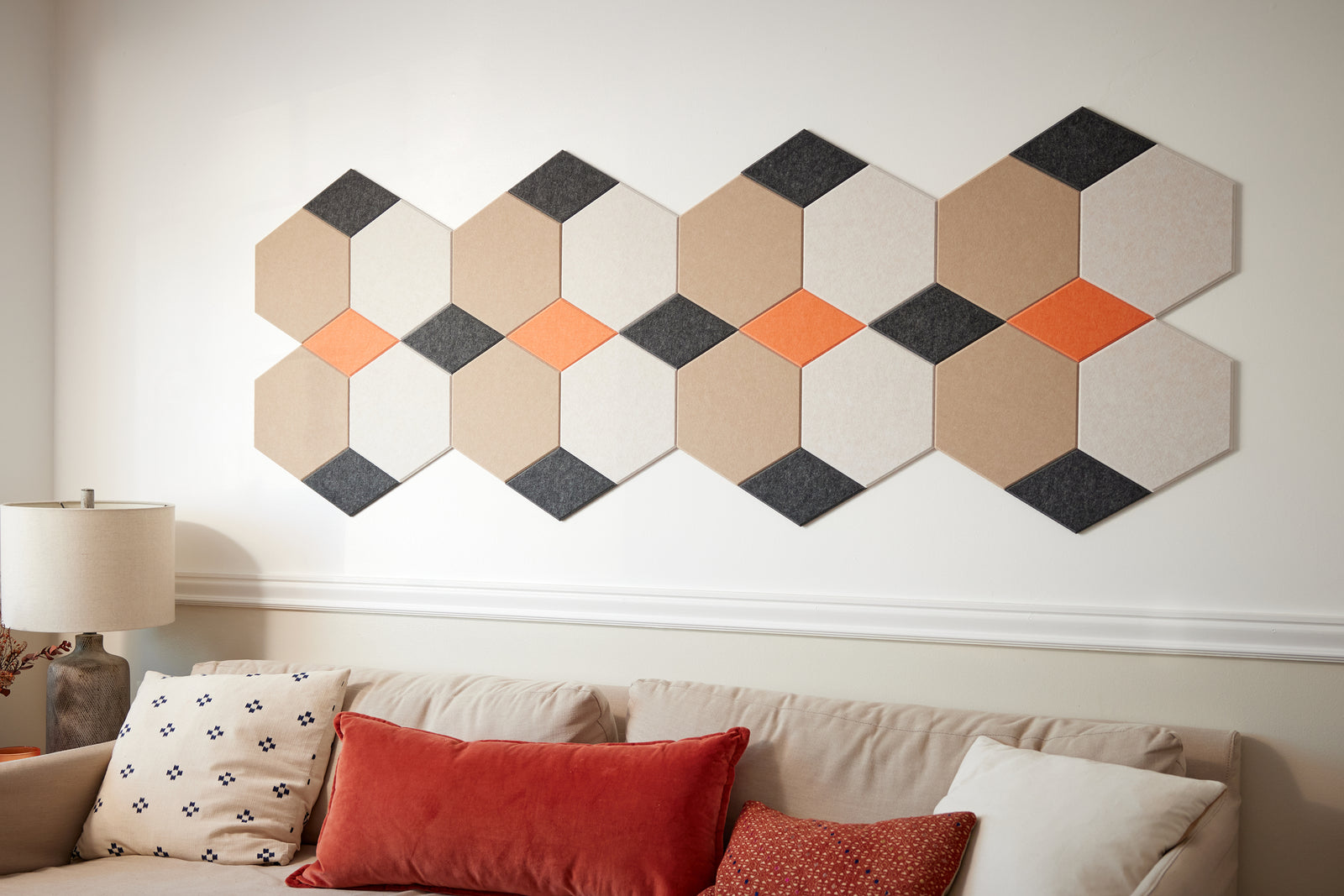 A Felt Right wall art design in shade of cream, orange, and black on light colored wall above a couch in a living room