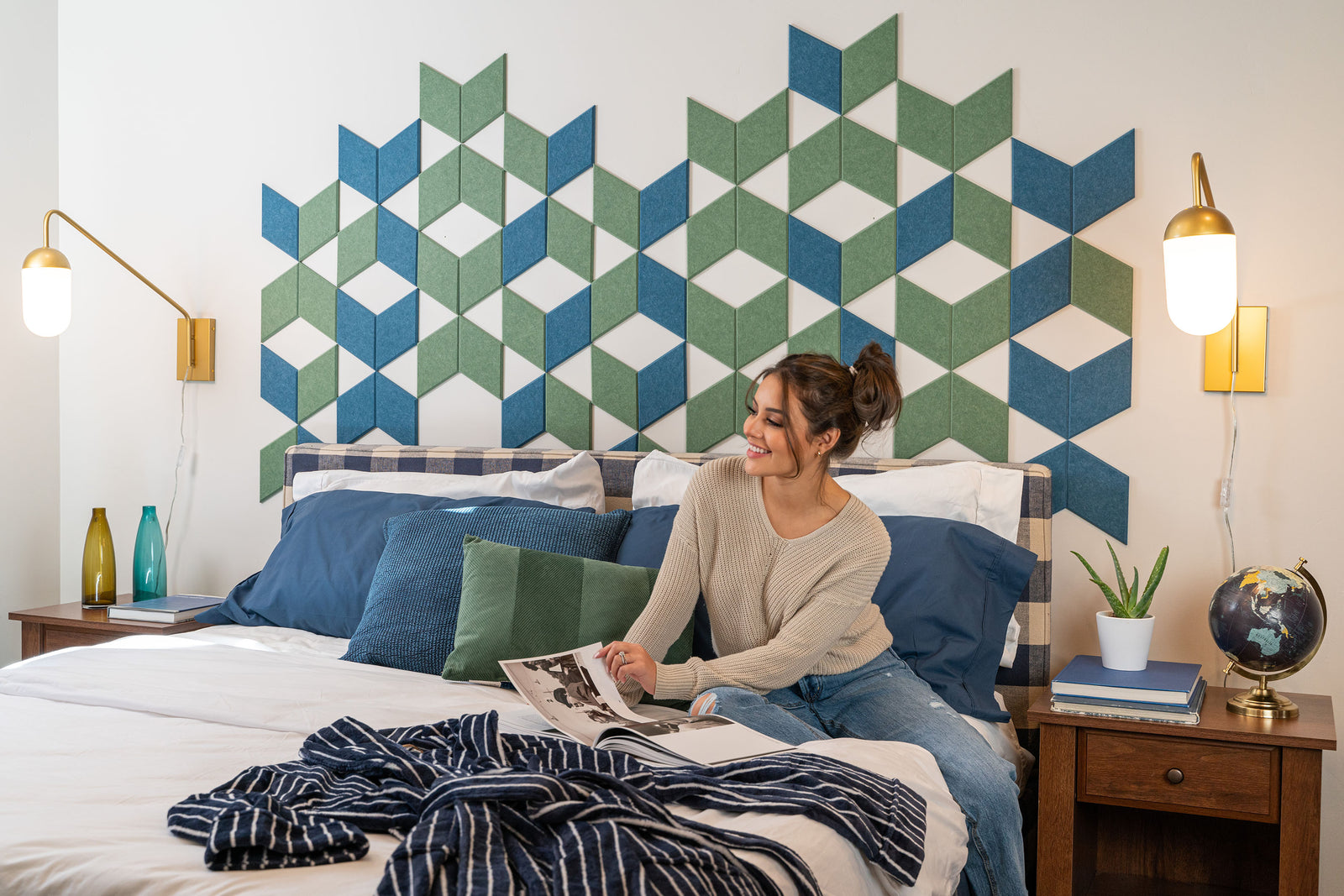 A Felt Right wall art design in shades of blue and green diamond felt tiles on a white wall in a bedroom behind a headboard of a bed.