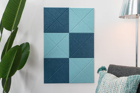 A Felt Right Wall design in light blue and dark blue checkered bulletin board board mounted on a wall in a home environment, with a lamp and a green plant to the side.