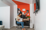A Felt Right wall art design in orange and black felt tiles on a white wall and ceiling behind a desk.