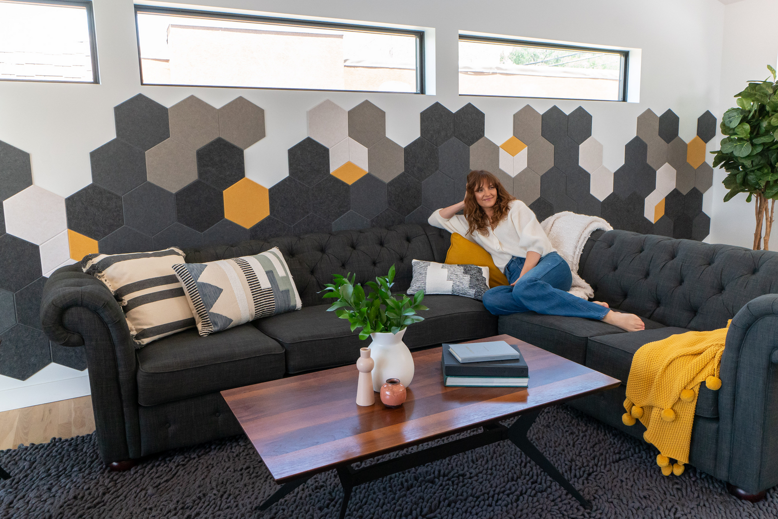 A Felt Right wall art design using shades of gray and yellow hexagons to create a honeycomb pattern along a wall behind a couch and a coffee table.