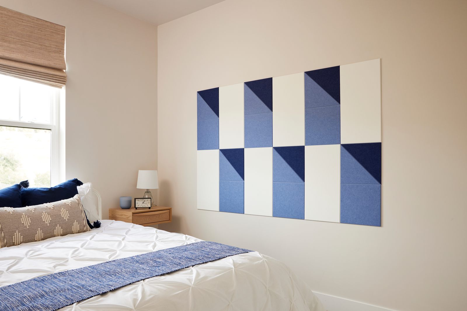 A Felt Right wall design using shades of blue and white next to a bed and night stand.