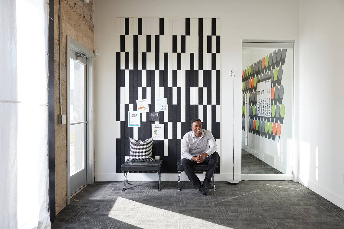 Felt Right wall art using black and white felt tiles to create a geometric pattern that is pinnable and on a white walls with two chairs in a waiting room with one man waiting
