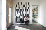 Felt Right wall art using black and white felt tiles to create a geometric pattern that is pinnable and on a white walls with two chairs in a waiting room with one man waiting