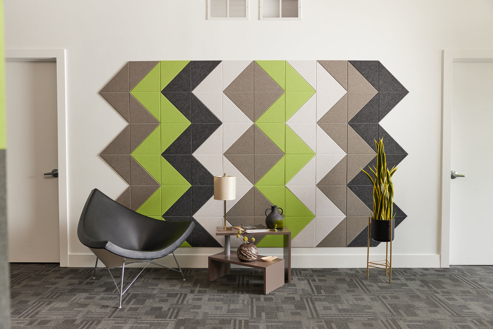 A Felt Right wall art design using shades of brown green and gray felt  on a white wall with a chair and a side table in front.