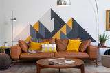 A Felt Right wall design wall decor featuring a geometric mountain-like pattern in shades of gray, black, and yellow, mounted on a wall above a brown sofa with yellow and gray throw pillows.