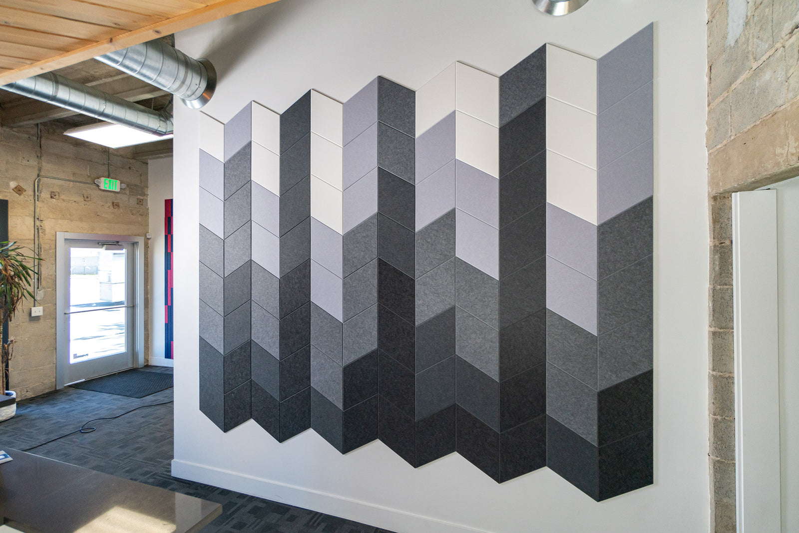 A Felt Right wall art design in shades of black, grey, and white in a geometric pattern on a white wall in an office building.