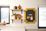 Felt Right wall art tiles in shades of black and yellow creating a framed look to pin card, photos, and to-do lists on a wall in a kitchen by shelves and windows