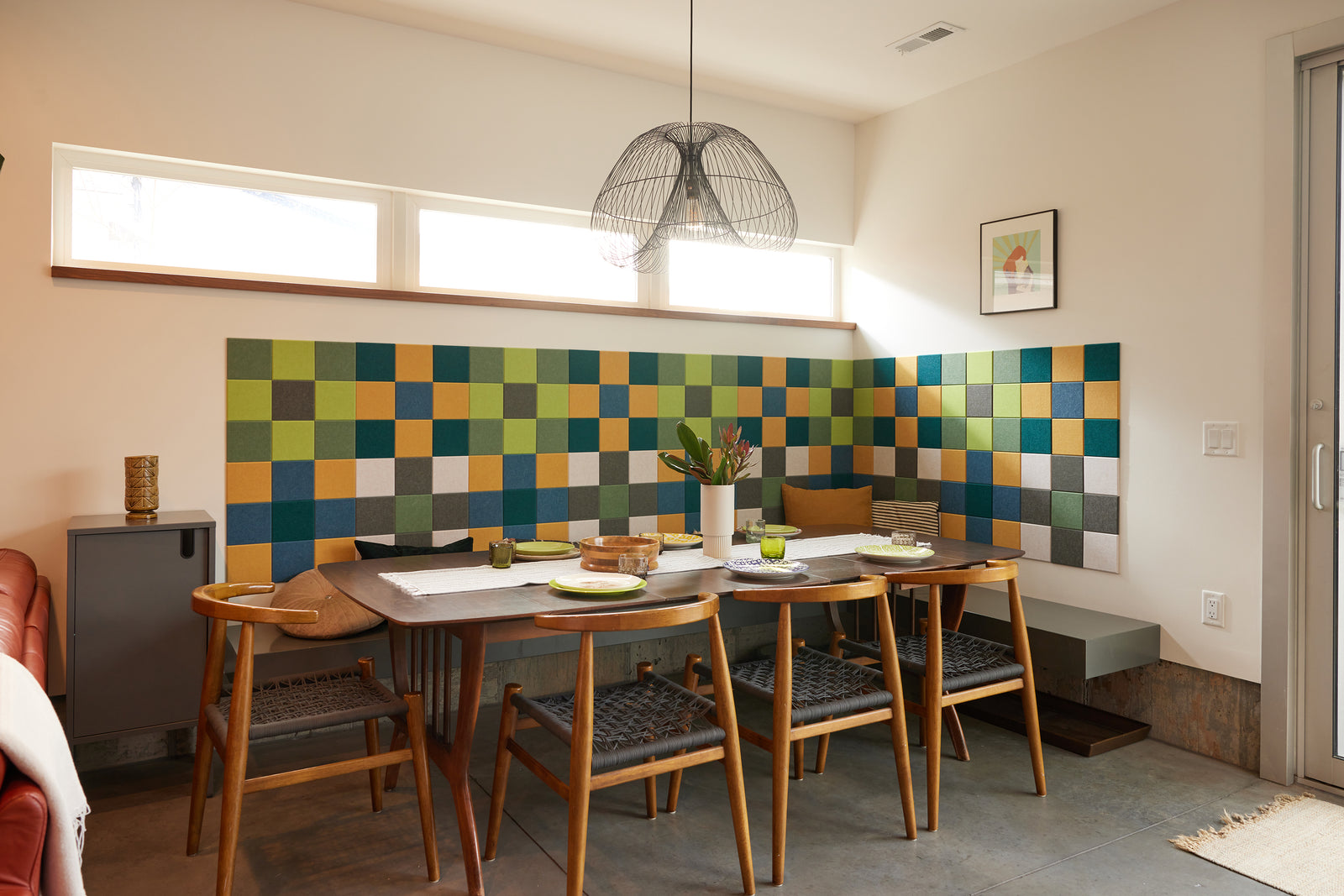 A Felt Right wall art design using shades of blue, green, yellow, and grey square felt tiles making a gingham patter along a wall by a kitchen table.