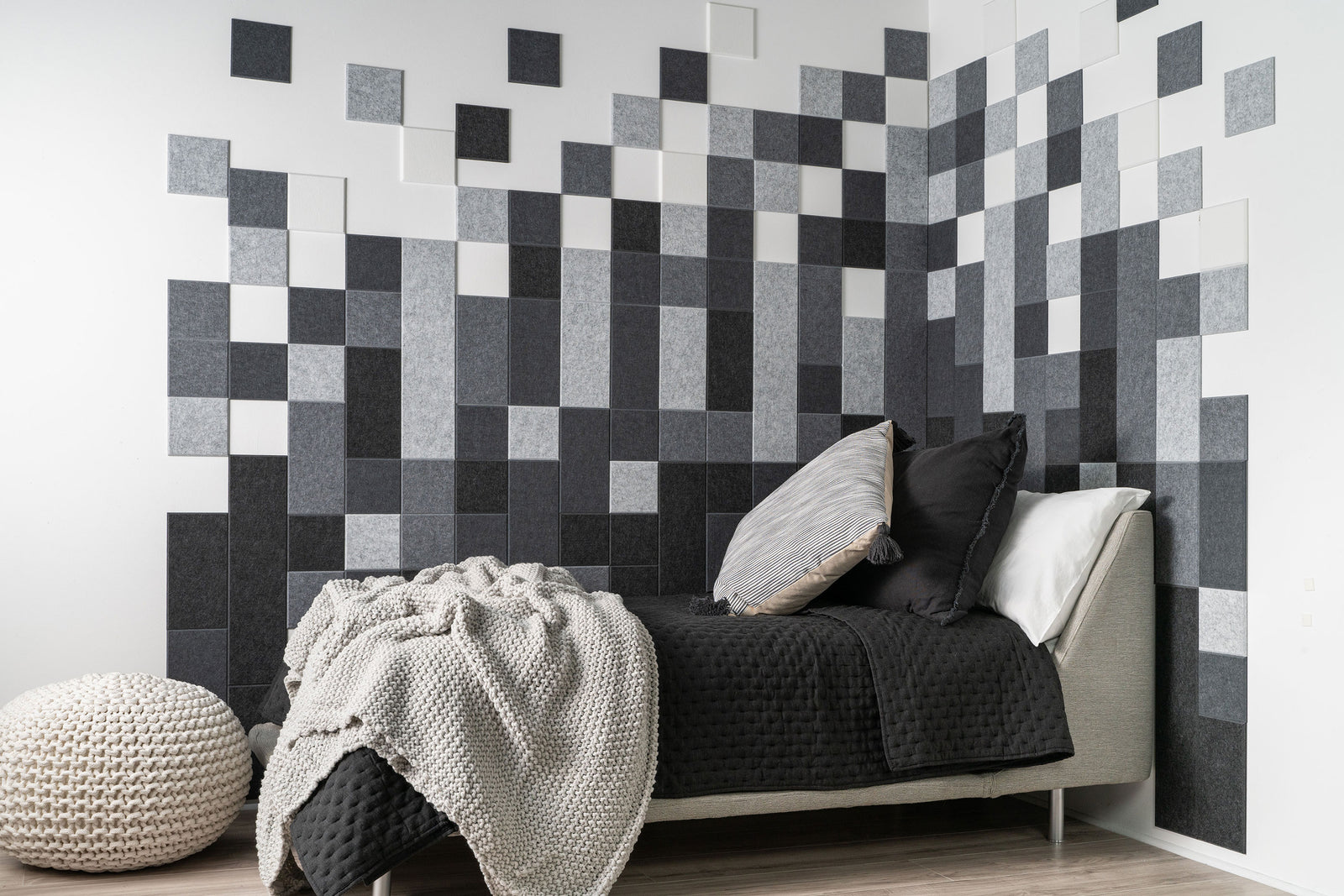 A Felt Right wall art design in shades of grey creating a geometric pixelated shapes in a corner of a bedroom with a bed.