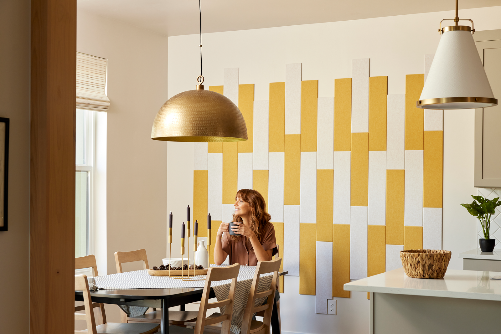 Felt Right wall art design using yellow and cream felt tiles in a shiplap look on a wall in a kitchen with a woman sitting at the kitchen table