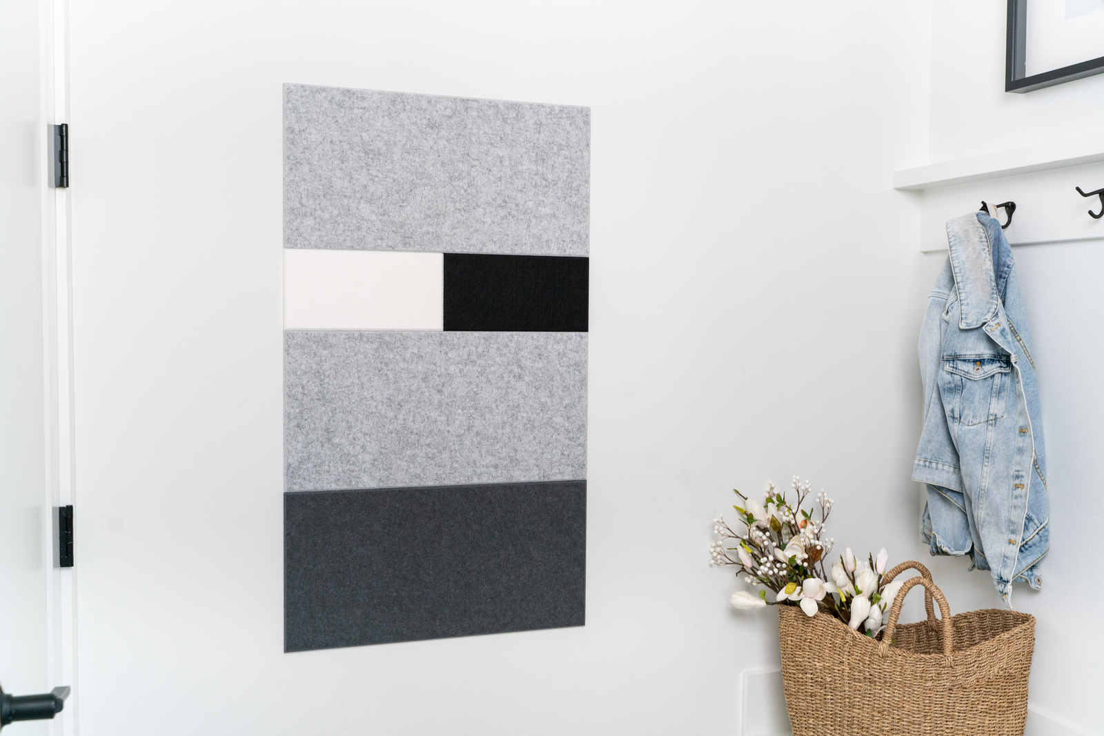 A Felt Right wall art design next to a door and a coat rack in shades of grey, black, and white next to a basket with flowers