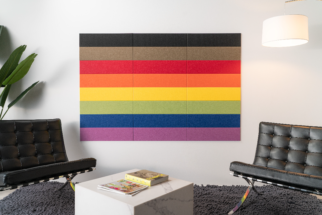 A Felt Right wall art design in multicolors creating the pride symbol in between two chairs and a small coffee tables.