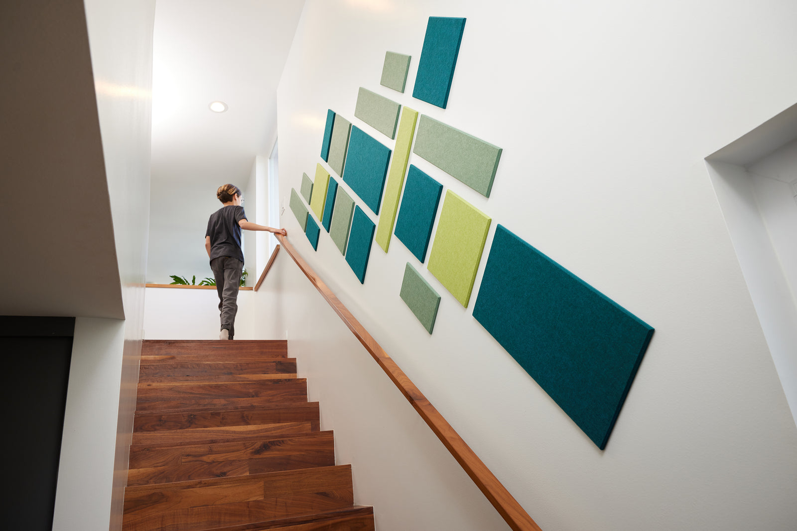 A Felt Right wall art design in shades of blue and green  creating a geometric shape on a wall along the stairs with a kid looking out the window.