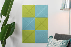 A Felt Right wall design made of felt and used as bulletin board with checkered shaped frames in blue and green shades, mounted on a wall next to a lamp and a plant.