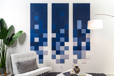 A Felt Right wall art design in blue pixelated squares on a white wall next to a chair with a decorative pillow and house plant.