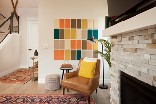 A room with a Felt Right color palette wall art, featuring shades of yellow, orange, red, and green, positioned above a white chair and a side table with a lamp.