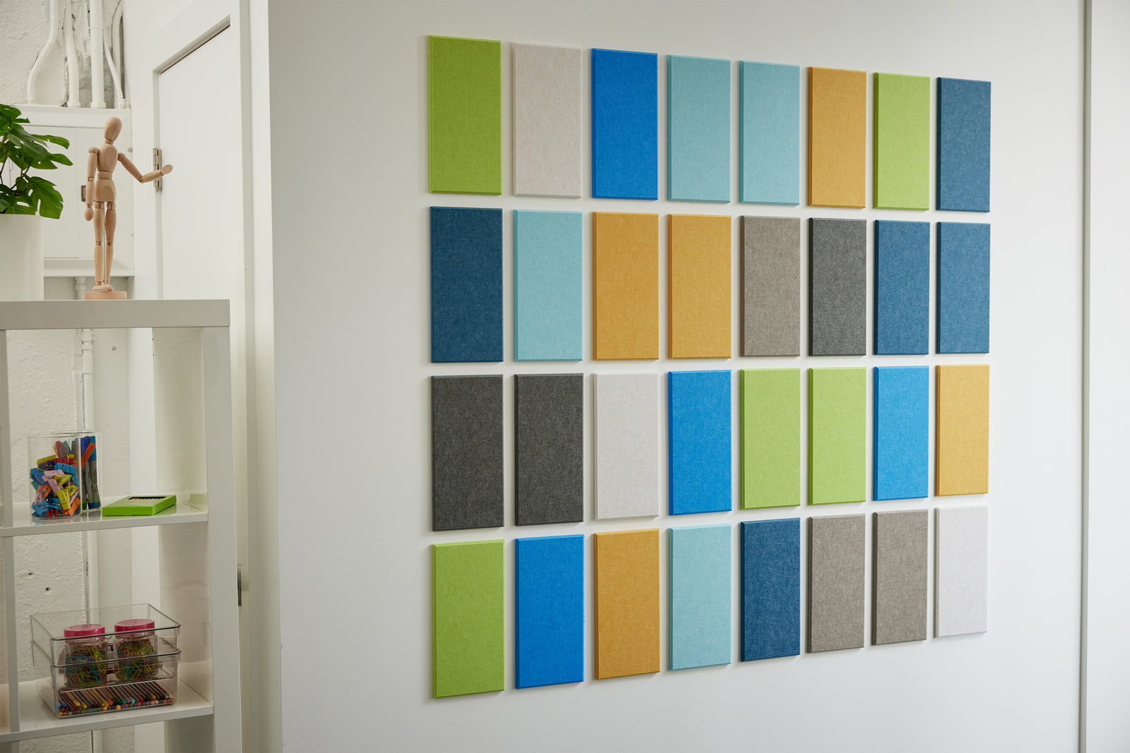 A Felt Right Wall Art design in shades of blue green grey white and yellow felt tiles next to a shelf.