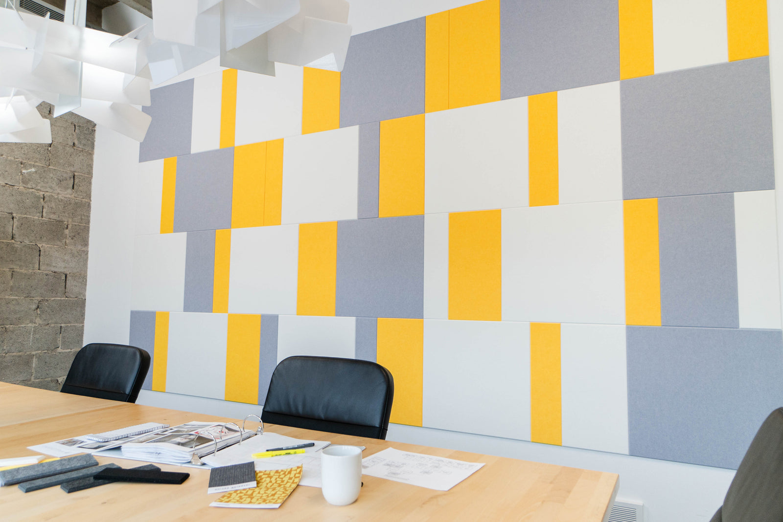 A Felt Right wall art design in shades of white yellow and grey felt tiles on a white wall in a conference room.