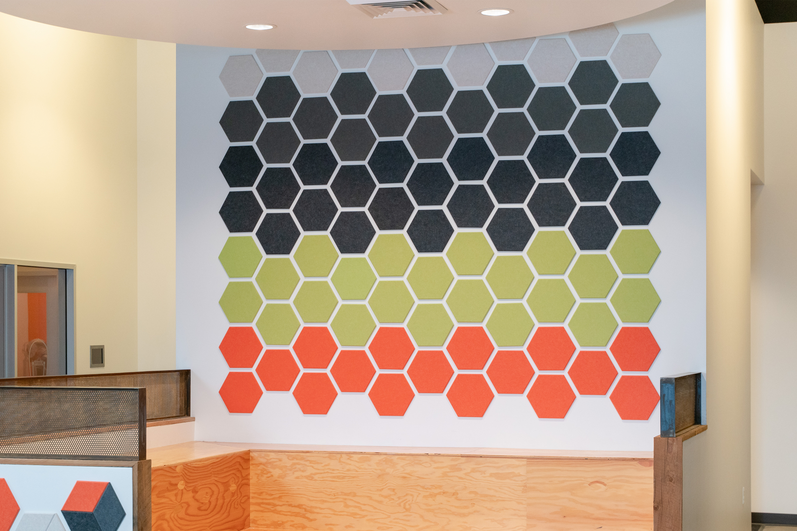 A Felt Right wall art design in shades of orange, green, and grey using hexagon shapes creating a pattern on a white wall in an office space.