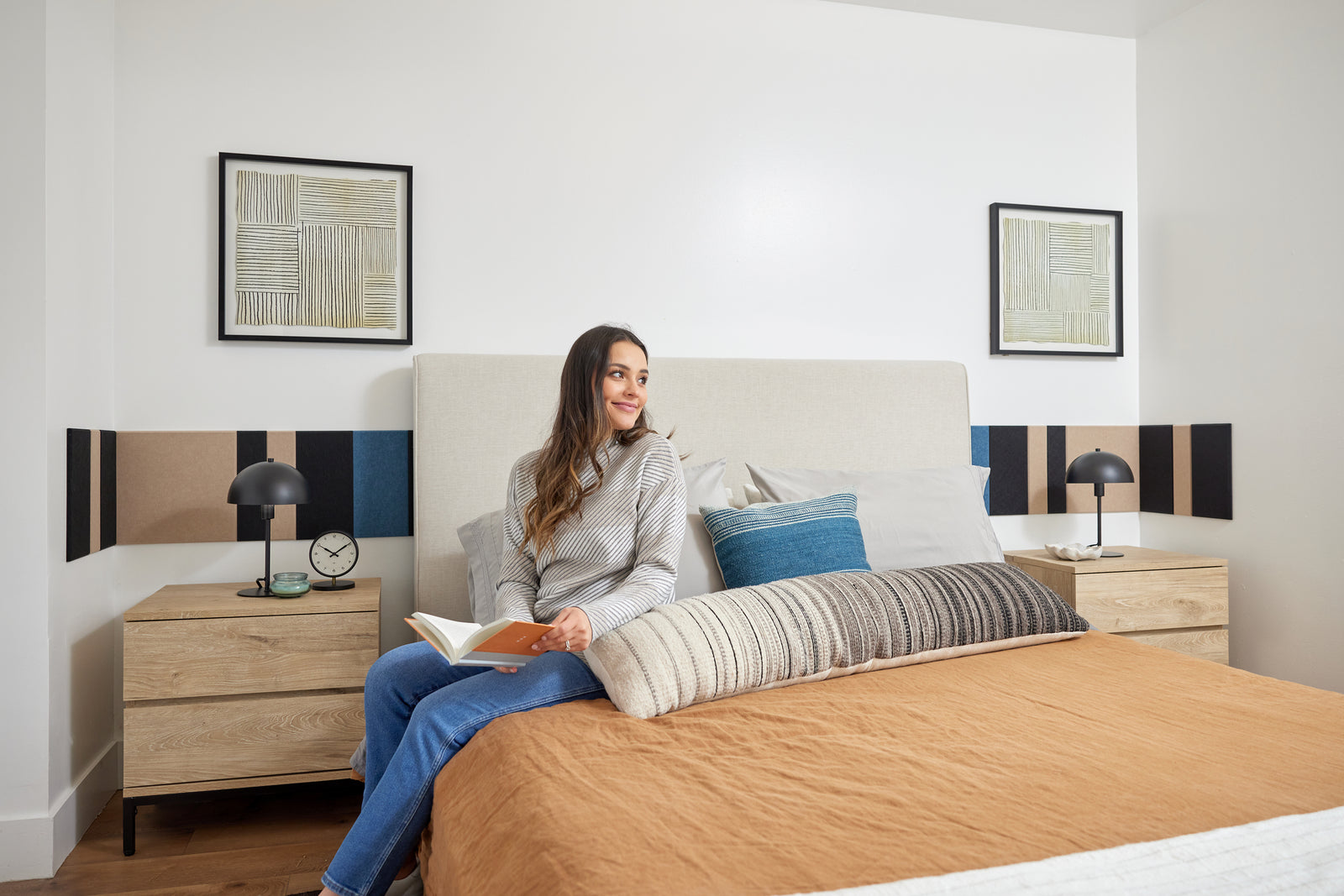 A Felt Right wall design in shades of black, cream, and blue in a strip pattern going along a wall behind a bed and side tables.