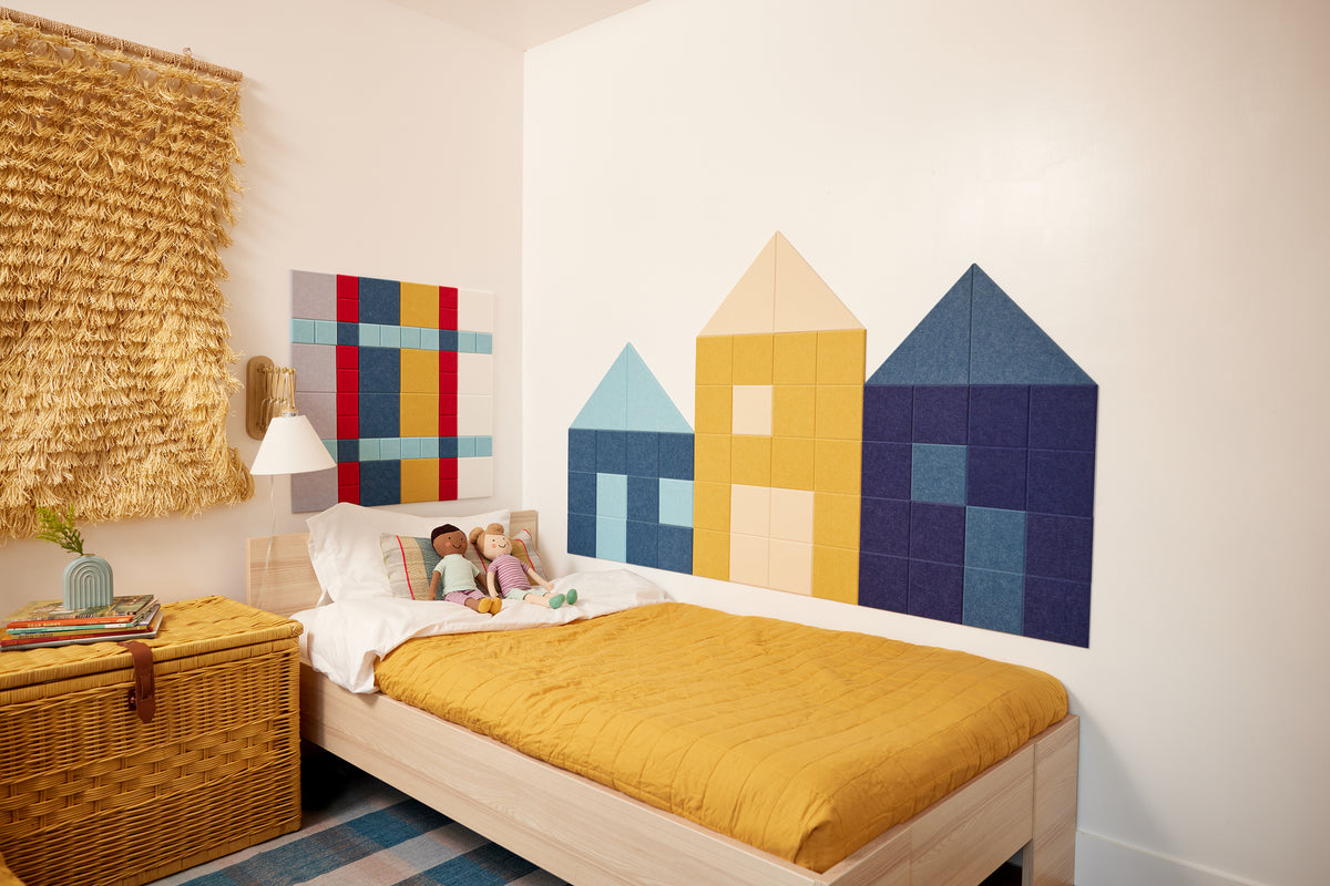 Felt Right wall art design to look like three houses in a row in shades of blue, yellow, and purple felt tiles in a kids bedroom alnog the bedside of the kids bed